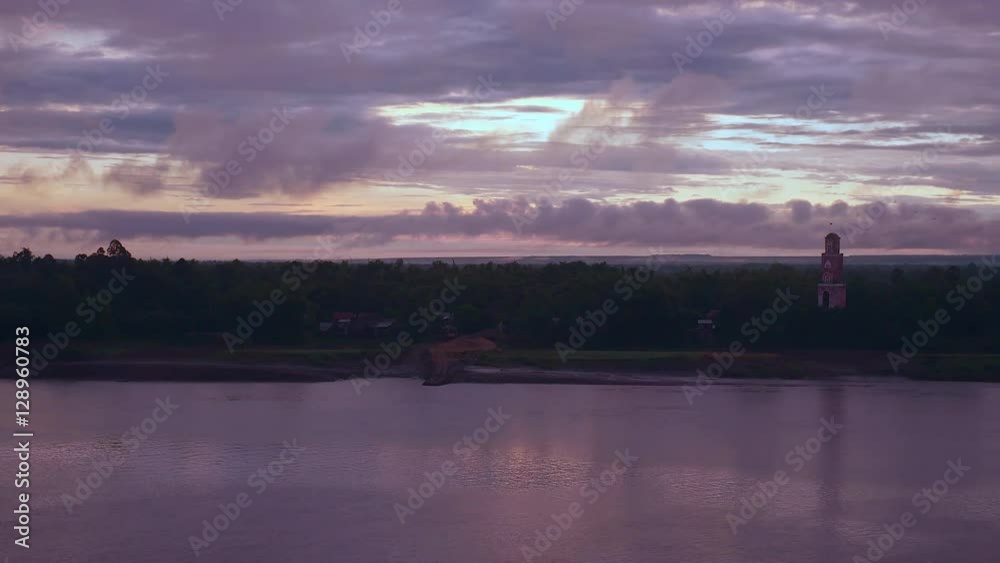 Wide bruised purple sunrise sky reflecting on river; Lookout tower rising by the riverside in the background Wide bruised purple sunrise sky reflecting on river; Lookout tower rising by the riverside in the background