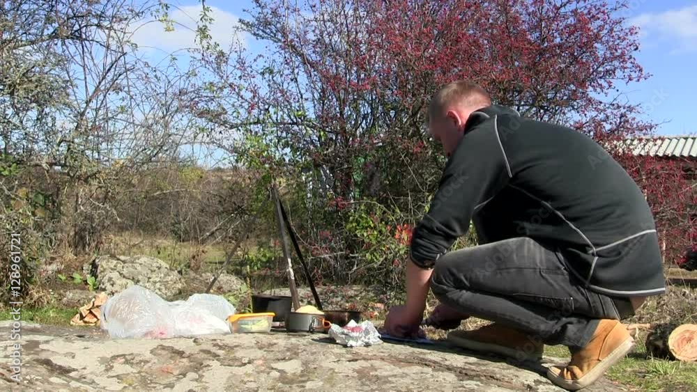
Cooking  food outdoors near bonfire. Man cuts meat
