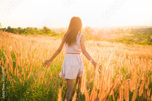 Beautiful girl in stylish summer dress walking in the field with flowers in sunlight,enjoying freedom feeling happy at sunset