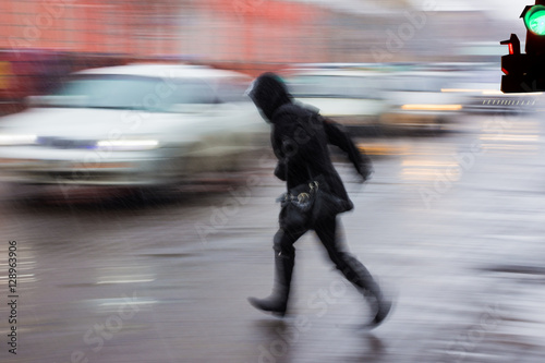 Woman on zebra crossing in a rainy day. Intentional motion blur
