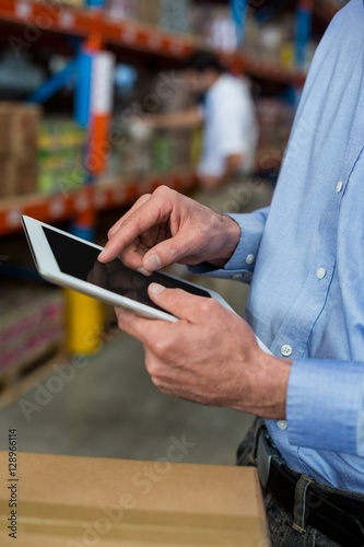 Mid section of warehouse worker using digital tablet