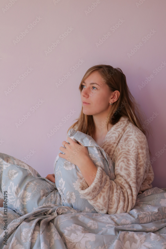 The girl blonde sitting in a bathrobe in the morning under a blanket The girl blonde sitting in a bathrobe in the morning under a blanket