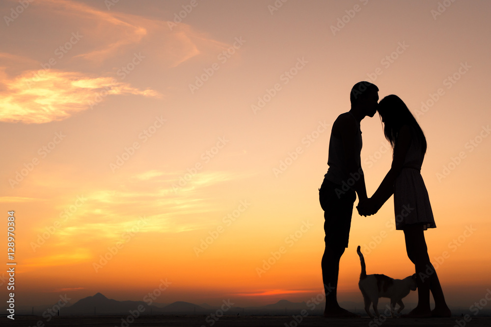 Silhouette of Happy Young Couple playing with cat Outside at Sunset