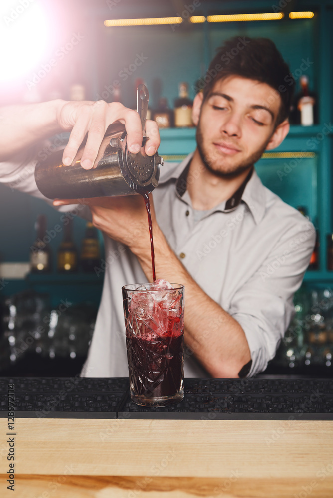 Young handsome barman pouring cocktail drink into glass