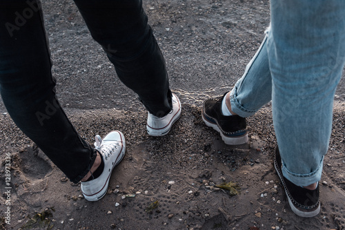 legs of two girls in jeans and sneakers on the lake at sunset