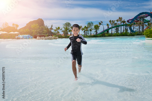 Fotografija laughing little boy jumping in a wetsuit on the water park.