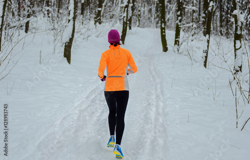 Winter running in forest: woman runner jogging in snow, outdoor fitness and sport concept, back view 