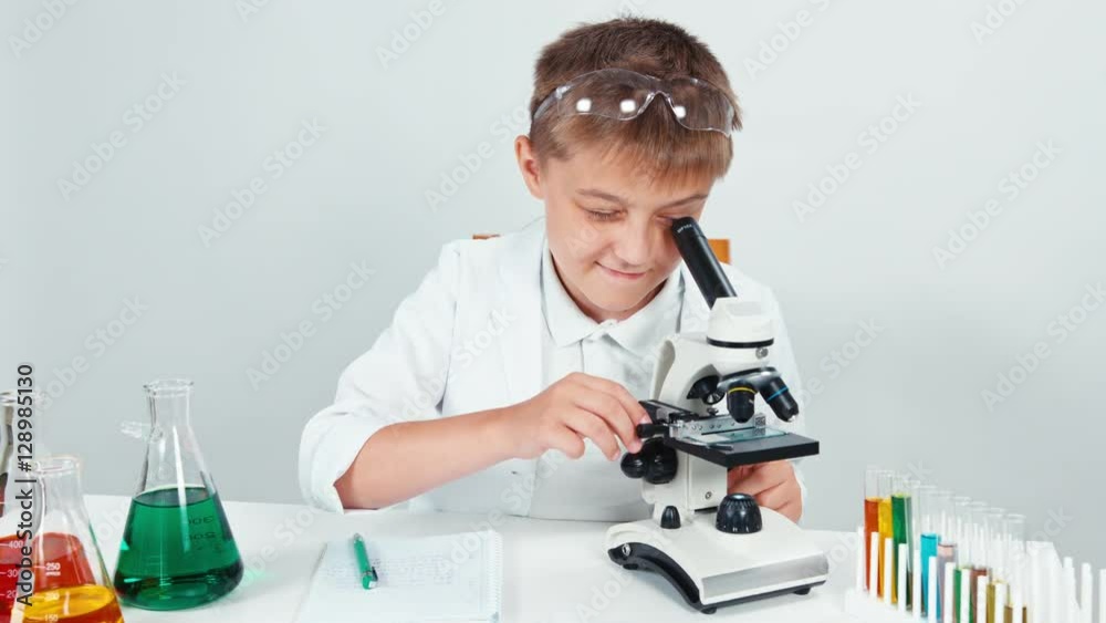 Chemist schoolboy 10-11 years old looking at microscope and smiling at camera isolated on white Chemist schoolboy 10-11 years old looking at microscope and smiling at camera isolated on white