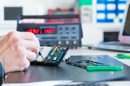 Closeup of hand of man sitting near computer and repairing cell phone