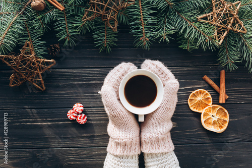 Female holding cup coffee, smartphone and christmas food on wooden background.