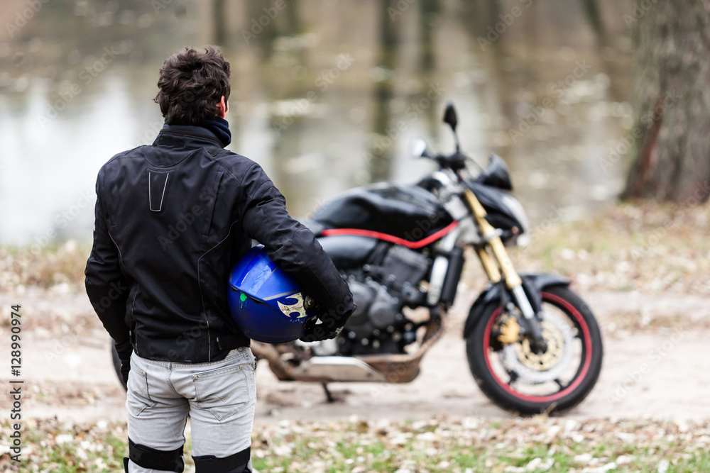 Biker standing near motorcycle, holding his blue helmet.