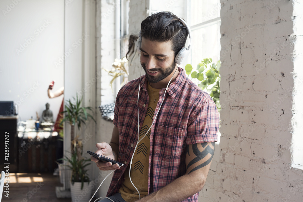 Smiling young man wearing headphones looking on cell phone in a loft Smiling young man wearing headphones looking on cell phone in a loft