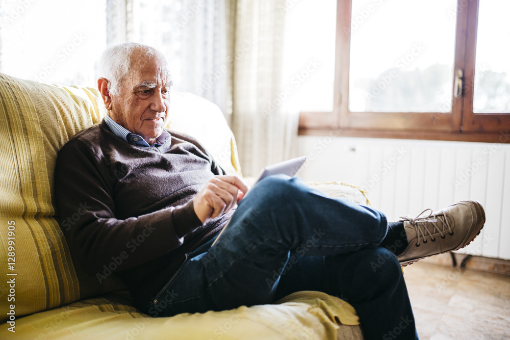 Senior man sitting on couch using tablet Senior man sitting on couch using tablet