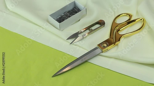 Tailor Puts Sewing Utensils on the Fabric - Scissors, Tailor's Cutter, Red and White Thread, Dressmaker Pins, Chalk and a Needle and Thread.