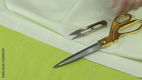 Tailor Puts Scissors and Tailor's Cutter on the Piece of Beige Fabric.