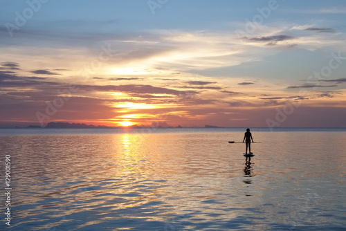 Paddleboarding at sunset. Silhouette of a young woman with cloudy landscape on the background. © Ilya Sviridenko