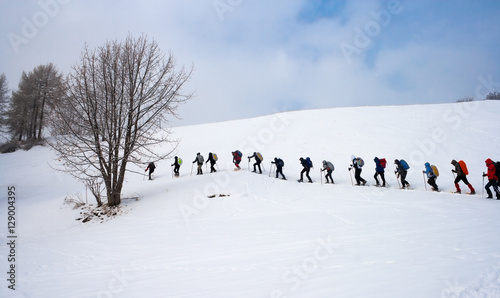 Persone in fila che camminano con le ciaspole in montagna