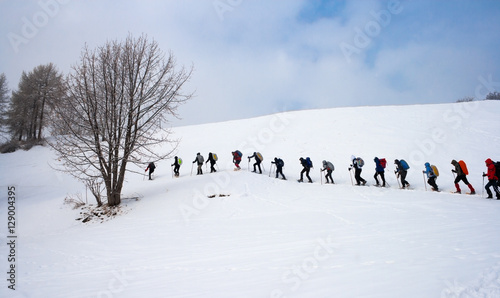 Persone in fila che camminano con le ciaspole in montagna photo