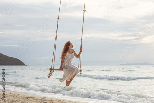 Beautiful young female sitting on the swing on sea shore