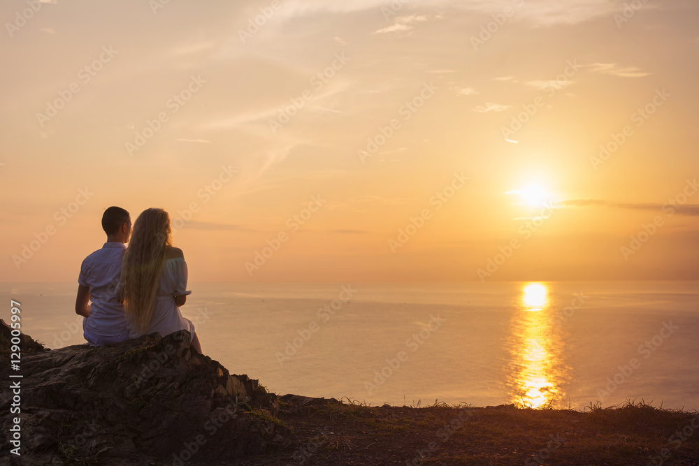 Young love couple sitting on the cliff and watching sunrise