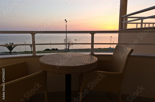 Table and two chairs on a balcony by the sea at sunrise in Greece