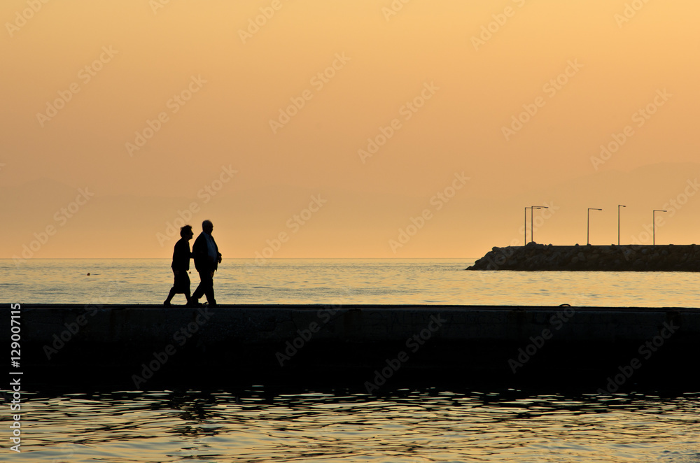 Grandpa and grandma on vacation walking on a pier by the sea at sunset in Chalkidiki, Greece