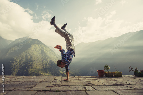 Fototapeta Young sporty man doing handstand exercise in beautiful mountain landscape