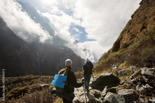 Girls with big backpack and trekking sticks walking in high mountains. Trekking in Himalayas, Nepal