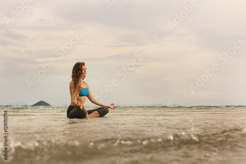 Young caucasian Woman sitting on sea shore and practicing yoga meditation. Enjoy ocean waves  wind and sun