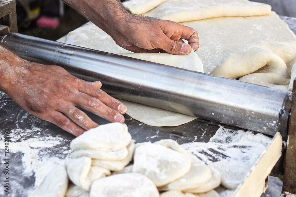 Fototapeta premium Chef making dough pastry sheeter at bakery Baker forming shaping dough rolled pastry metal work table closeup hands process of preparing bread khinkali dough roller machine thin pasta sheet Top view