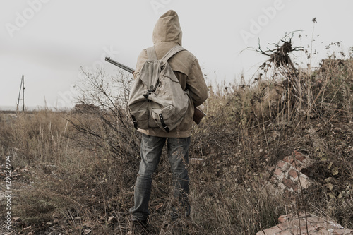 wandering boy. boy with a gun. boy goes to an abandoned building. boy stands in front of a building. Post apocalypse. Boy traveling on foot in a post-apocalyptic world in search of food. 