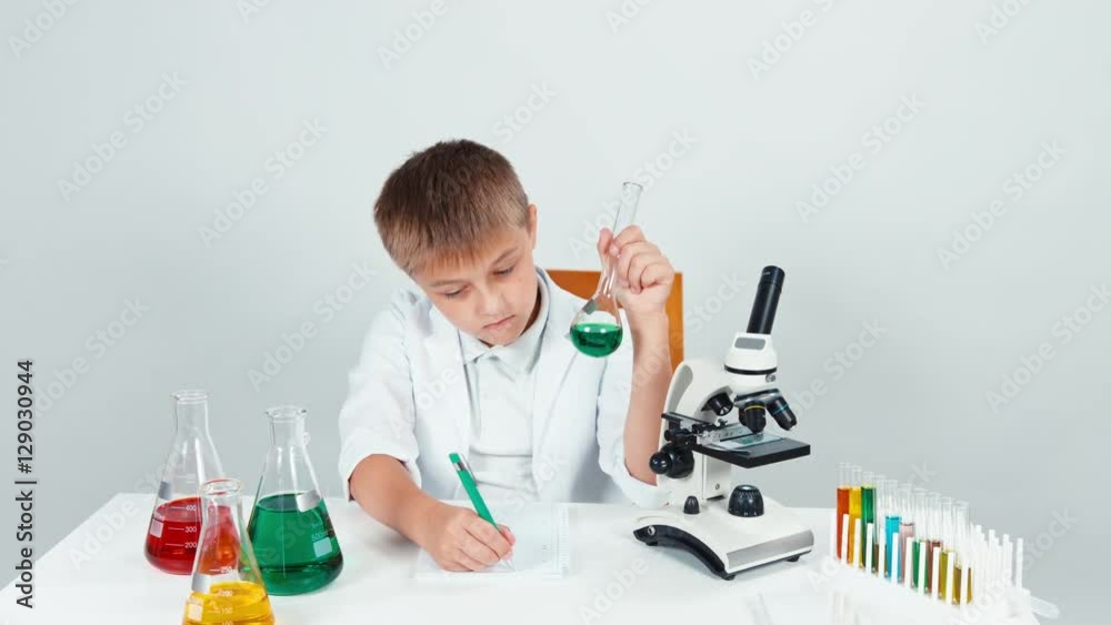 Portrait young chemist mixing chemicals. Schoolboy holding flask looking at it and writing in notebook Portrait young chemist mixing chemicals. Schoolboy holding flask looking at it and writing in notebook
