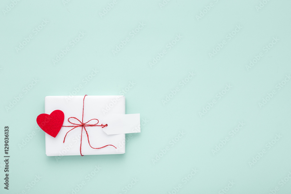 Valentine or birthday white gift with red bow,  blank label decorated with felt heart on pastel blue background. Valentines day. Flat lay. Copy space.