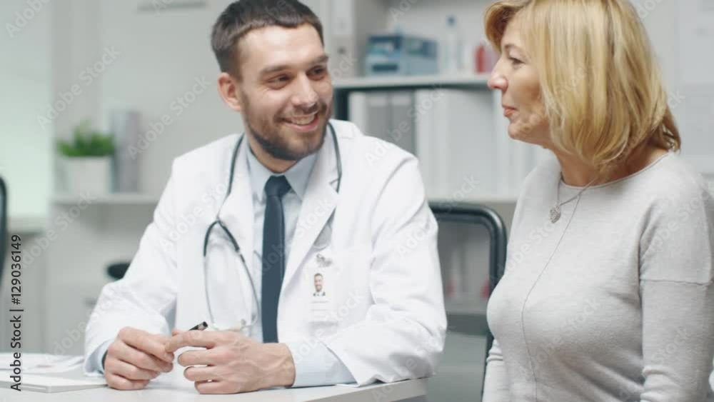 Male Doctor Consults Mid Adult Female Patient. They Talk and Smile. Shot on RED Cinema Camera in 4K (UHD). Male Doctor Consults Mid Adult Female Patient. They Talk and Smile. Shot on RED Cinema Camera in 4K (UHD).
