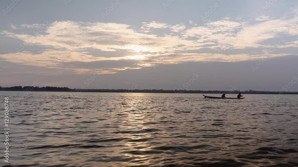 Small fisherman's dugout canoe on river under cloudy sunrise (shot from a moving boat) Small fisherman's dugout canoe on river under cloudy sunrise (shot from a moving boat)