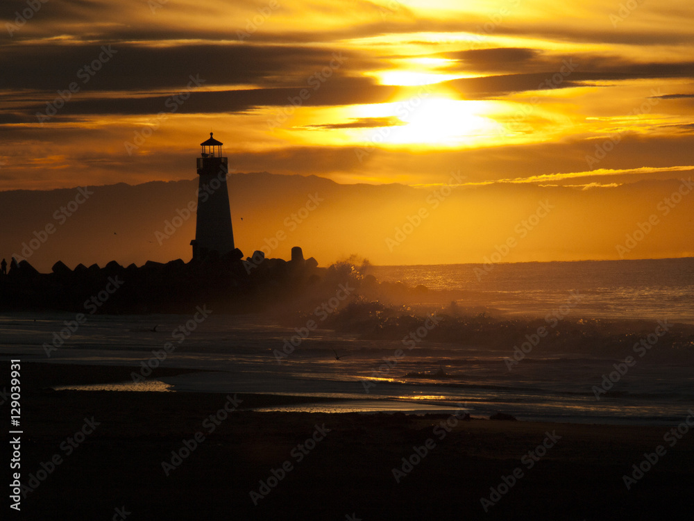 Lighthouse silhouette in sunrise with crashing waves