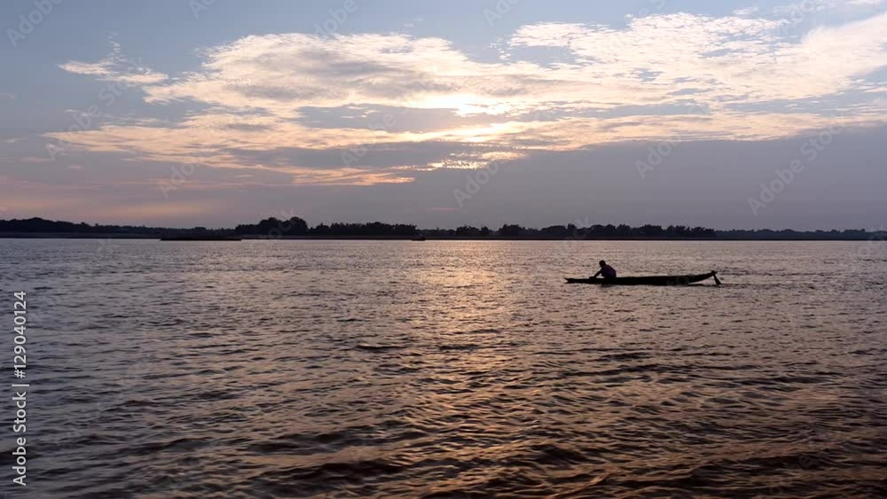 Small fisherman's dugout canoe on river under cloudy sunrise (shot from a moving boat) Small fisherman's dugout canoe on river under cloudy sunrise (shot from a moving boat)