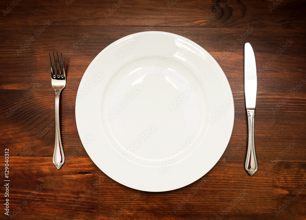 White plate with fork and knife on wooden table White plate with fork and knife on wooden table
