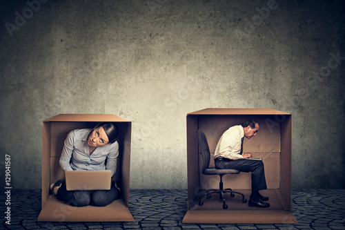 Introverts. Man and woman sitting inside boxes working on laptop