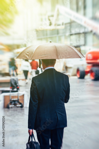 Businessman under rain walking toward sun