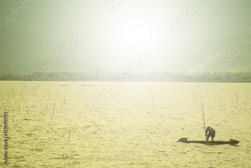 A fisherman is fishing in the big lake in Thailand by the afternoon with the sun flare by sepia style.