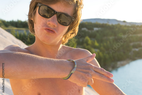 boy standing on the beach. boy looks into the distance. a boy in sunglasses. boy in swimming shorts. boy naked. boy on the white sand. boy near the azure sea. blue water.