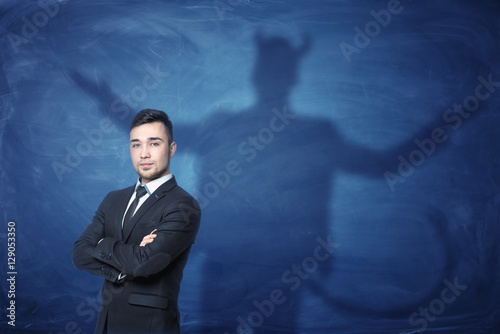 фотографія Businessman standing with hands across and his shadow on blue blackboard behind