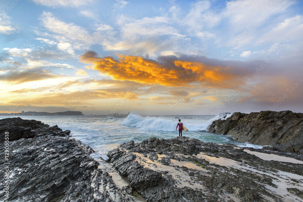 Surfer contemplating the ocean waves during sunset at Currumbin Rock, Gold Coast