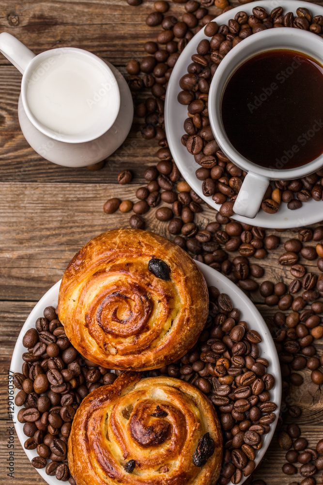 Coffee cup with milk jug and cinnabons on wooden background. Coffee cup with milk jug and cinnabons on wooden background.