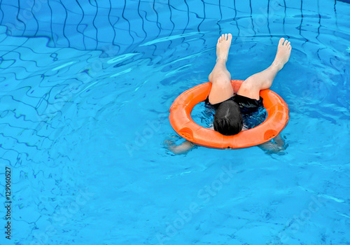 Little boy floating with an orange ring at the swimming pool