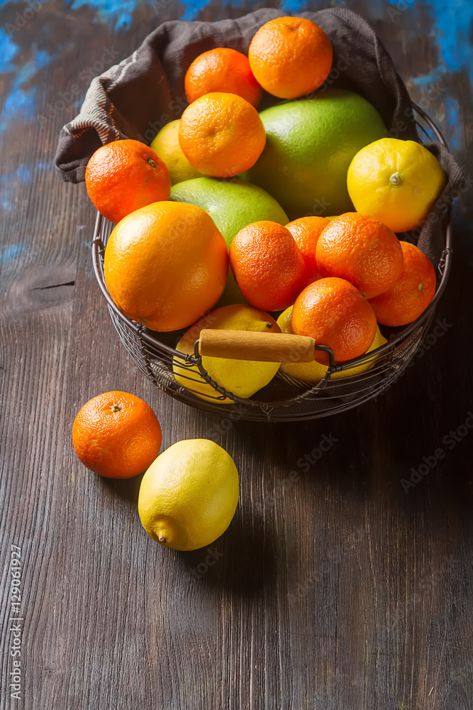 Different fresh citrus fruit in a basket on a wooden background.