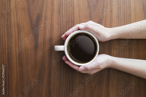 hands holding white coffee cup and hot espresso coffee on wooden table. top view
