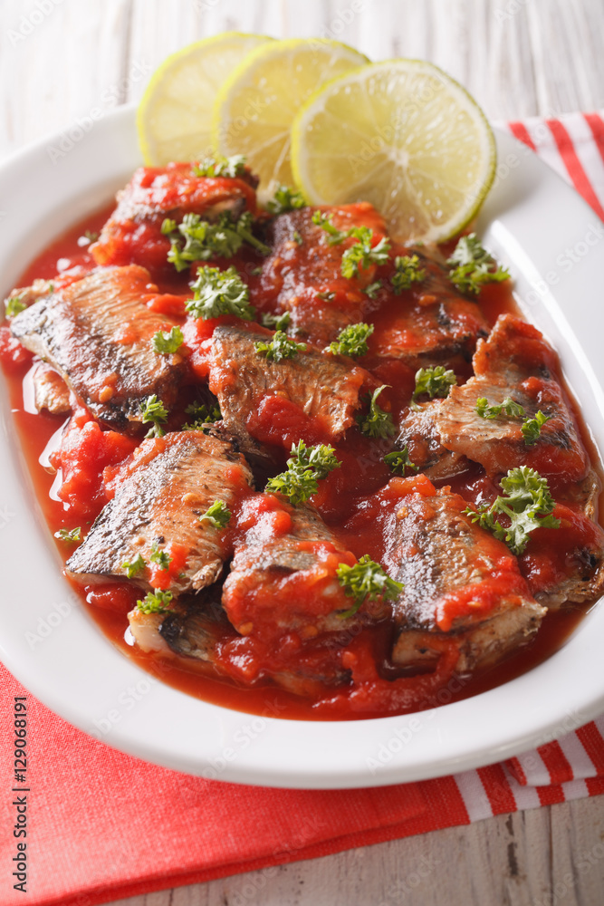 Braised sardines in tomato sauce with lime and parsley close-up. Vertical Braised sardines in tomato sauce with lime and parsley close-up. Vertical