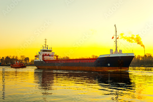 Tugboat assisting cargo ship in port at sunrsie.
